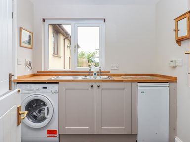 A small utility room with a washing machine a sink under a window and a small refrigerator at Hole Park in Holsworthy
