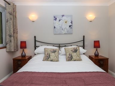 A bedroom with a double bed two bedside tables with lamps and a floral painting on the wall at Hole Park in Holsworthy