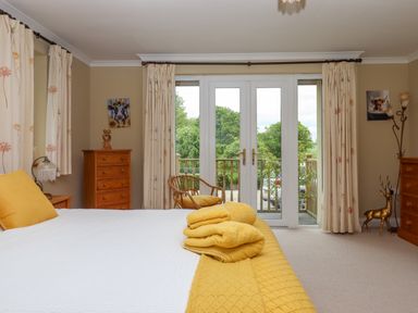 A bedroom with a bed and yellow bedding next to double glass doors leading outside at Hole Park in Holsworthy