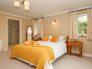 A bedroom with a double bed covered with white bedding and yellow pillows and blanket beside wooden nightstands and windows at Hole Park in Holsworthy