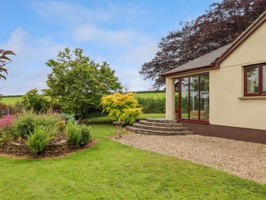 A garden with plants and trees next to a house with stone steps and gravel at Hole Park in Holsworthy