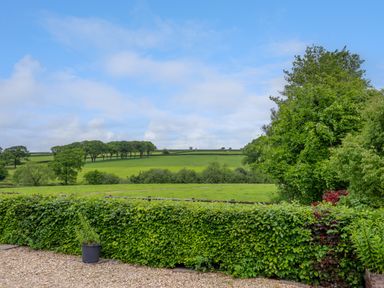 A garden with hedges and potted plants overlooking green fields and trees at Hole Park in Holsworthy