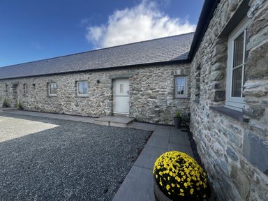 An outdoor view of a stone building with a door at Beudy Tanrallt in Llanfachraeth