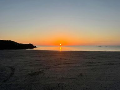 A beach with a sunset over the ocean at Beudy Tanrallt in Llanfachraeth