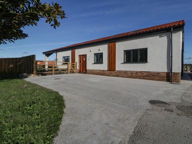 A single-story building with a red tiled roof a wooden door two windows a wooden fence and a concrete driveway at Hidden Well in Aust