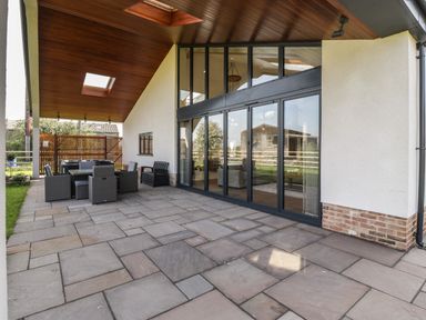 A covered outdoor patio area with stone flooring glass sliding doors and outdoor furniture at Hidden Well in Aust