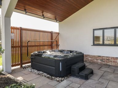 A covered outdoor patio with a hot tub next to a wooden fence and a window at Hidden Well in Aust