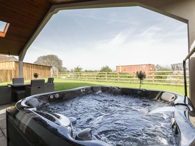 A covered outdoor space with a hot tub and a patio table with chairs at Hidden Well in Aust
