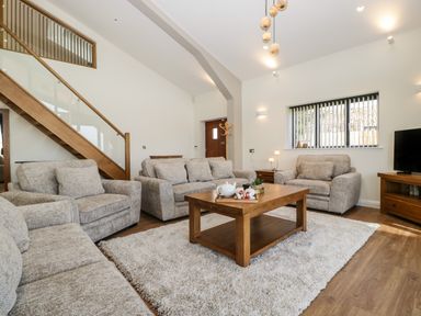 A living room with three gray sofas a wooden coffee table a TV on a stand and a staircase at Hidden Well in Aust