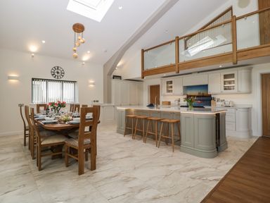 A kitchen and dining area with a wooden dining table set for a meal and a kitchen island with bar stools at Hidden Well in Aust
