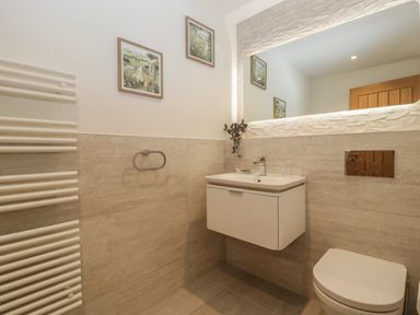 A bathroom with a mounted sink, toilet, heated towel rail, and framed pictures on the wall at Hidden Well in Aust
