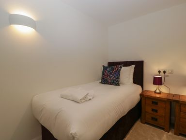 A bedroom with a single bed white bedding a pillow and folded towels next to wooden bedside tables with a lamp at Hidden Well in Aust
