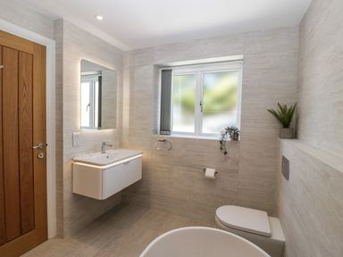 A bathroom with a wooden door floating sink with a mirror window toilet and plants at Hidden Well in Aust