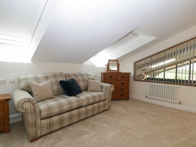 An attic room with a plaid sofa and wooden dresser with a mirror at Hidden Well in Aust