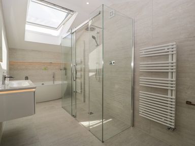 A bathroom with a glass shower enclosure a bathtub a wall-mounted sink and a white towel radiator at Hidden Well in Aust