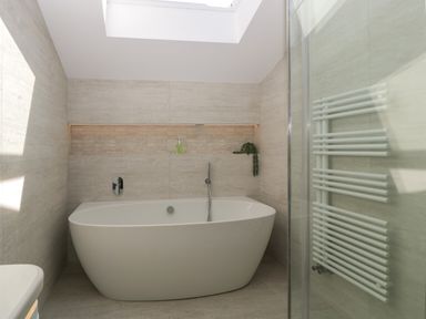 A bathroom with a freestanding bathtub a wall-mounted faucet a skylight and a towel radiator at Hidden Well in Aust