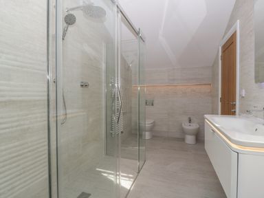 A bathroom with a walk in shower glass doors a toilet bidet and a sink with a wooden door at Hidden Well in Aust