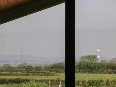 A view of green fields and trees with a bridge and electrical tower in the distance at Hidden Well in Aust