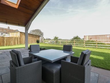 An outdoor patio with a square table and four chairs under a wooden roof at Hidden Well in Aust