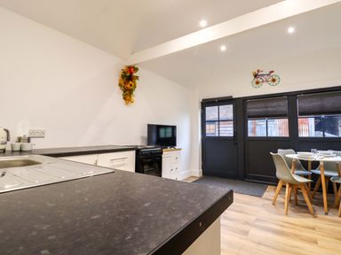 A kitchen with a countertop stove a dining table with chairs and a door with windows at Kingfisher Cottage Ottinge near Lyminge