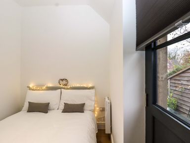 A bedroom with a bed with white bedding and two gray pillows next to a window with a black blind at Kingfisher Cottage in Ottinge near Lyminge