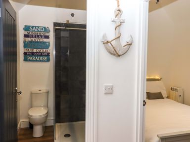 A bathroom with a toilet and glass shower next to a bedroom with a bed and pillow at Kingfisher Cottage in Ottinge near Lyminge