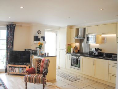 A kitchen with cream cabinets a stove microwave coffee machine and a striped armchair at 5 Thurlestone Beach in Thurlestone