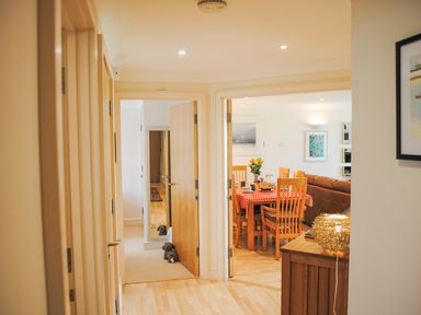 A hallway leading to a dining room with a table and chairs and a room with a door and mirror at 5 Thurlestone Beach in Thurlestone