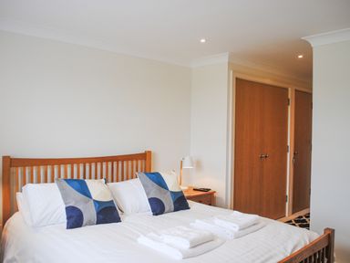 A bedroom with a wooden bed frame two pillows with geometric design bedside table with lamp and folded towels at 5 Thurlestone Beach in Thurlestone
