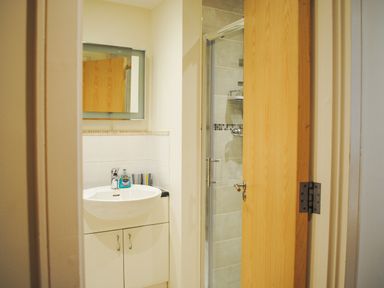 A bathroom with a white sink and cabinet a mirror and a partially open wooden door leading to a shower at 5 Thurlestone Beach in Thurlestone