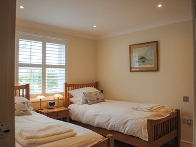 A bedroom with two single beds a wooden nightstand with two lamps and a clock and a framed picture on the wall at 5 Thurlestone Beach in Thurlestone