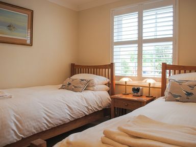 A bedroom with two single beds and a wooden nightstand with lamps at 5 Thurlestone Beach in Thurlestone