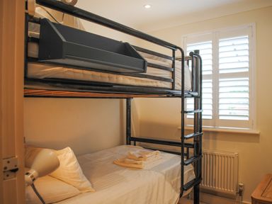 A bedroom with a black metal bunk bed a window with white shutters and a bedside lamp at 5 Thurlestone Beach in Thurlestone