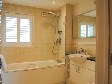 A bathroom with a bathtub and shower next to a window and a sink with cupboard below at 5 Thurlestone Beach in Thurlestone