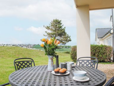 An outdoor patio table with flowers muffins mugs and bowls with a view of green hills and houses at 5 Thurlestone Beach in Thurlestone