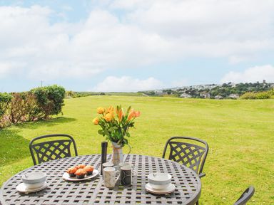 A metal outdoor table set with muffins mugs and flowers on a lawn overlooking houses at 5 Thurlestone Beach in Thurlestone