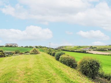 A grassy field with trimmed bushes and a building in the distance at 5 Thurlestone Beach in Thurlestone