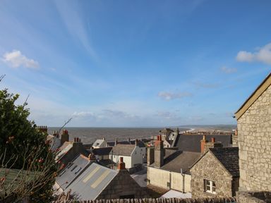 Rooftops of stone and brick houses overlooking the sea under a blue sky at Cove Cottage Hideaway in Chiswell On Portland