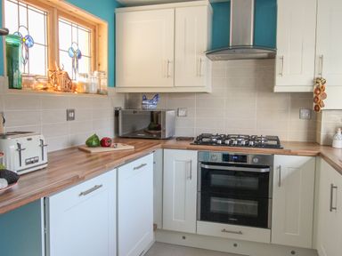 A kitchen with white cabinets wooden countertop a microwave a gas stove a toaster and stained glass window at Cove Cottage Hideaway in Chiswell On Portland