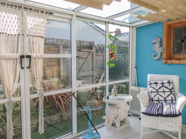 A sunroom with wicker chair and table next to glass doors overlooking a garden at Cove Cottage Hideaway in Chiswell On Portland