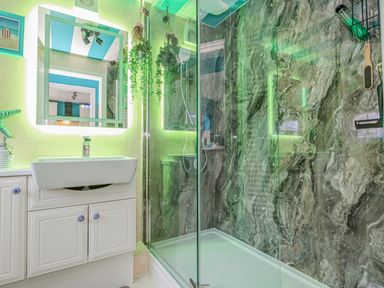 A bathroom with a white sink and cabinet a glass shower enclosure and green lighting at Cove Cottage Hideaway in Chiswell On Portland