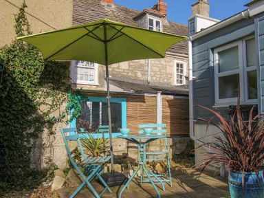 An outdoor patio with turquoise chairs and table under a green umbrella with stone walls at Cove Cottage Hideaway in Chiswell On Portland