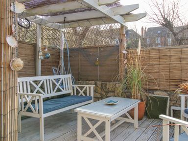 An outdoor seating area with white wooden bench and table under a pergola with bamboo fencing at Cove Cottage Hideaway in Chiswell On Portland