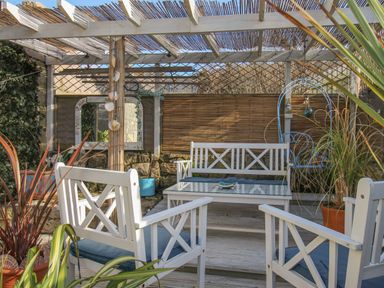 An outdoor seating area with white wooden chairs a white wooden bench a glass top table and plants under a pergola at Cove Cottage Hideaway in Chiswell On Portland