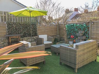An outdoor seating area with wicker furniture and a green umbrella at Cove Cottage Hideaway in Chiswell On Portland