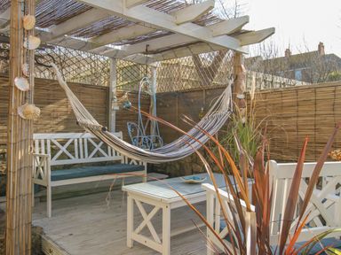 An outdoor seating area with a hammock a bench a wooden table and decorative plants at Cove Cottage Hideaway in Chiswell On Portland