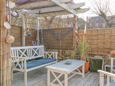 A patio with white wooden bench and table with blue cushions under a pergola at Cove Cottage Hideaway in Chiswell On Portland