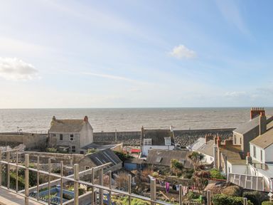 A coastal village with houses gardens and a sea wall along the shore at Cove Cottage Hideaway in Chiswell On Portland