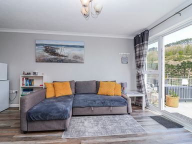 A living room with a sofa and shelves at Shells Cottage in Looe