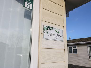 A close-up of a beige exterior wall with a sign reading A and C Lodge Plot 21 and a green caravan number 21 sign at A and C Lodge-Plot 21 in Armathwaite